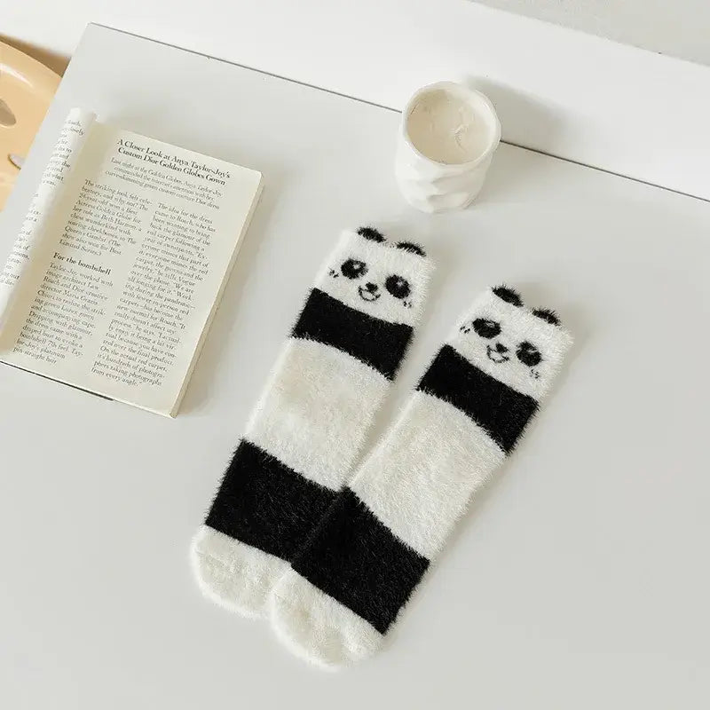 Kósýsokkar - Hvítir og svartir with cute panda design on a table next to a candle and an open book, perfect for cozy home wear.