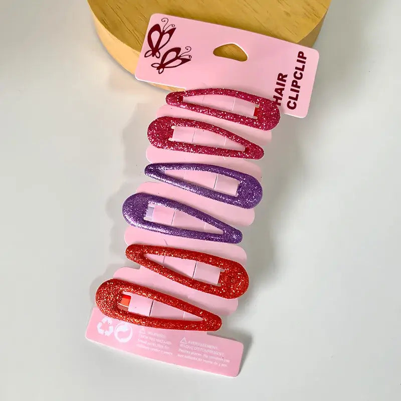 Hárspennur - Glimmer 6 stk on a display card, featuring red and purple glitter hair clips. Stylish accessories for any occasion.