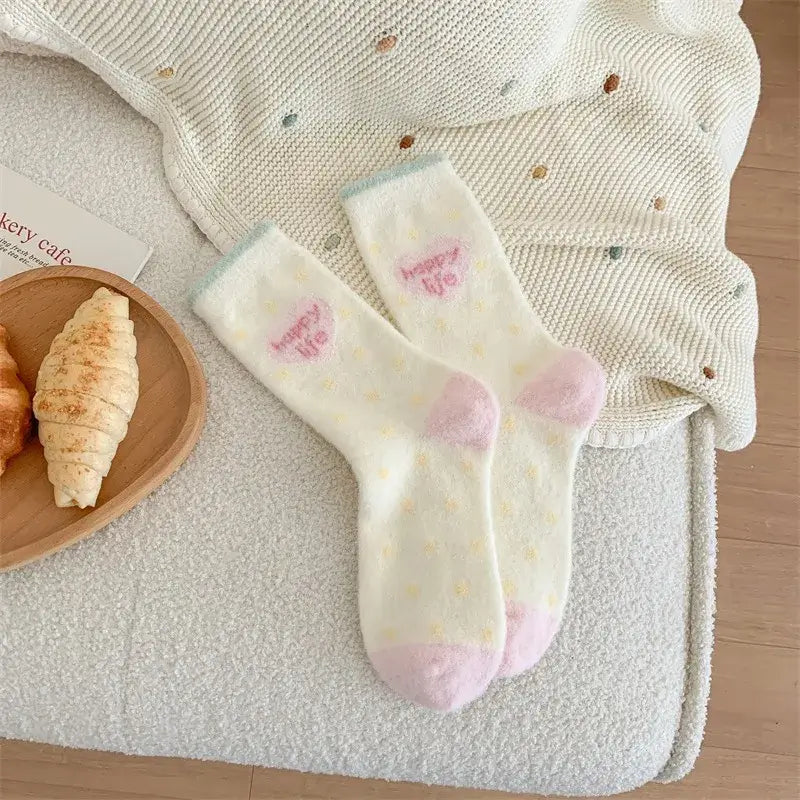 Kósýsokkar - hvítir og bleikir með röndum og teiknimyndahöfði á teppi við hliðina á croissant á borði.